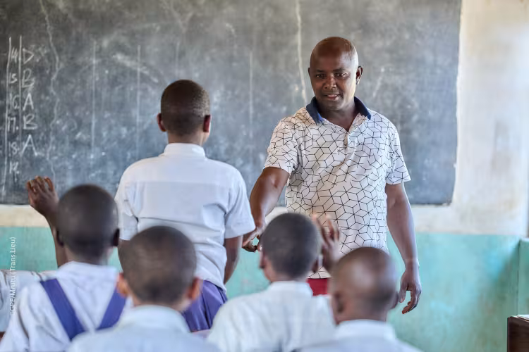 Male teacher interacting with students in a classroom in Tanzania.