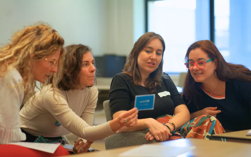 Four women looking at a blue card and discussing.