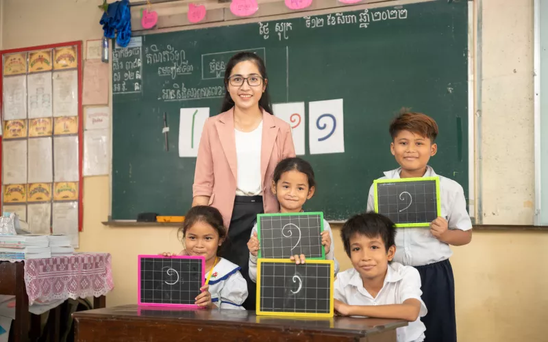 A teacher and four smiling students hold chalkboards with maths equations. 