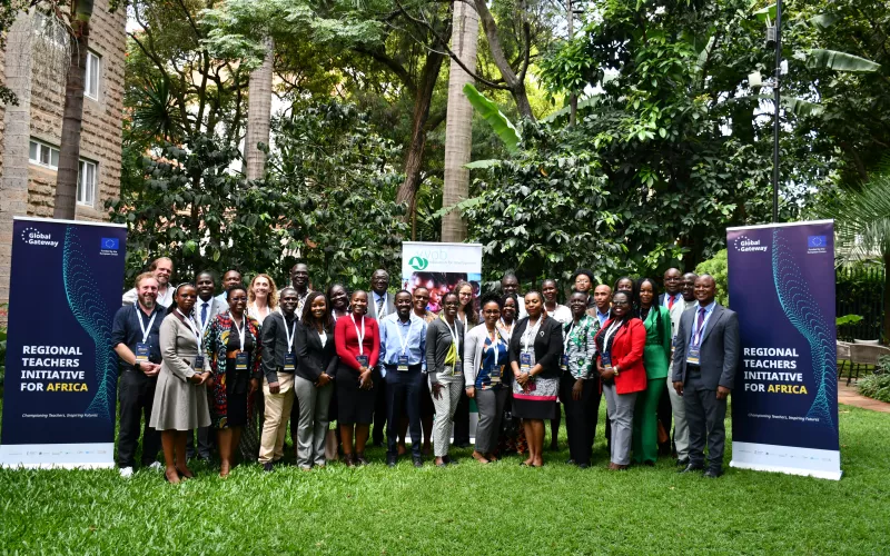 A diverse group of people standing on grass, smiling, next to two large banners.