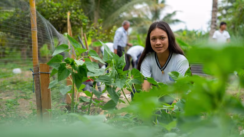 A student in Ecuador looks at the camera while tending to an agricultural project
