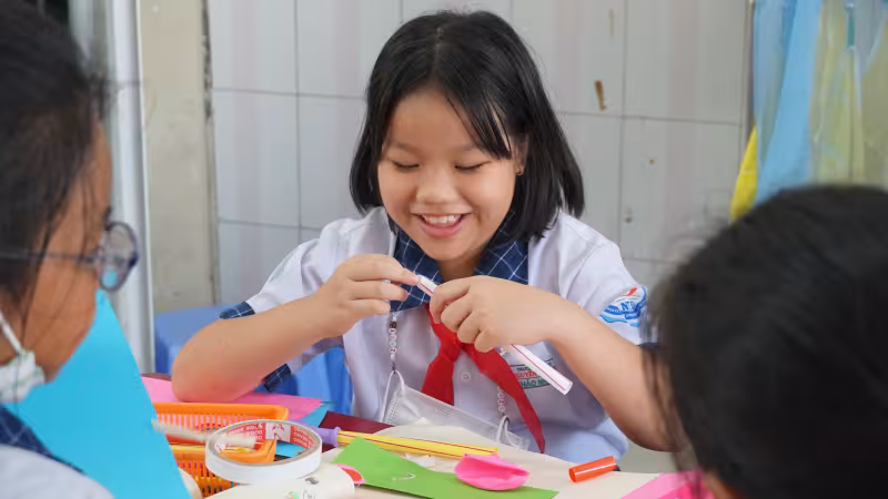 Vietnamese student enjoys playing with coloured papers and art supplies
