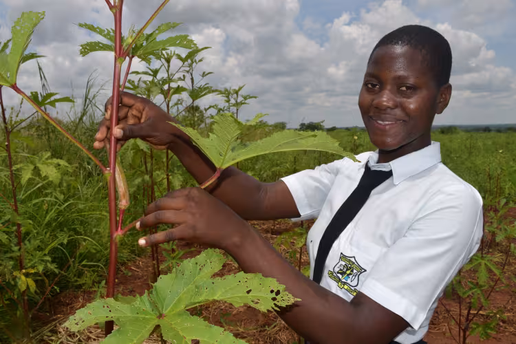 An agricultural student in Uganda poses with a plant