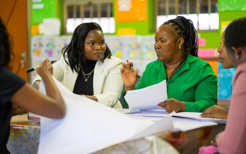 Female eachers sit together at a classroom table discussing notes during a professional learning community.