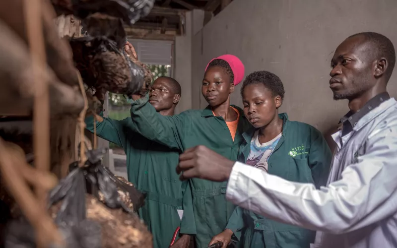 Three students in green overalls being guided by an instructor.