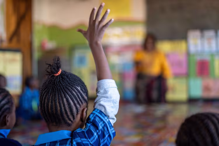 A schoolgirl raises her hand in a classroom in Zambia