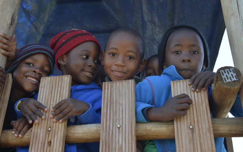 Four young children smile and lean on a wooden fence.