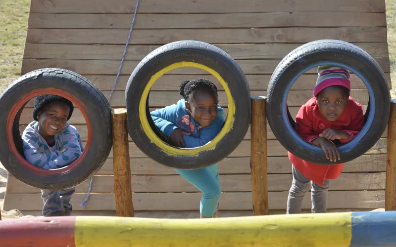 Three children smiling and looking through the opening of a car tire while posing for the camera