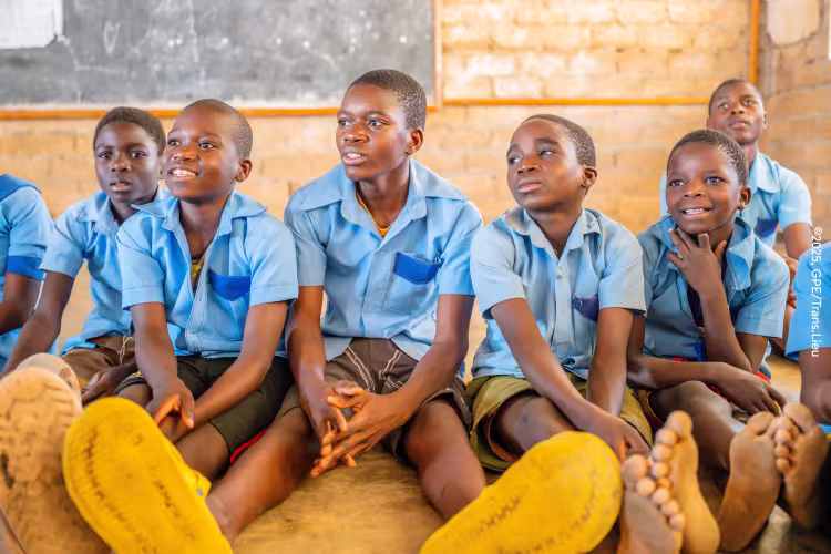 African schoolchildren in blue uniforms sit together in a classroom, smiling and listening attentively in a warm, joyful scene.