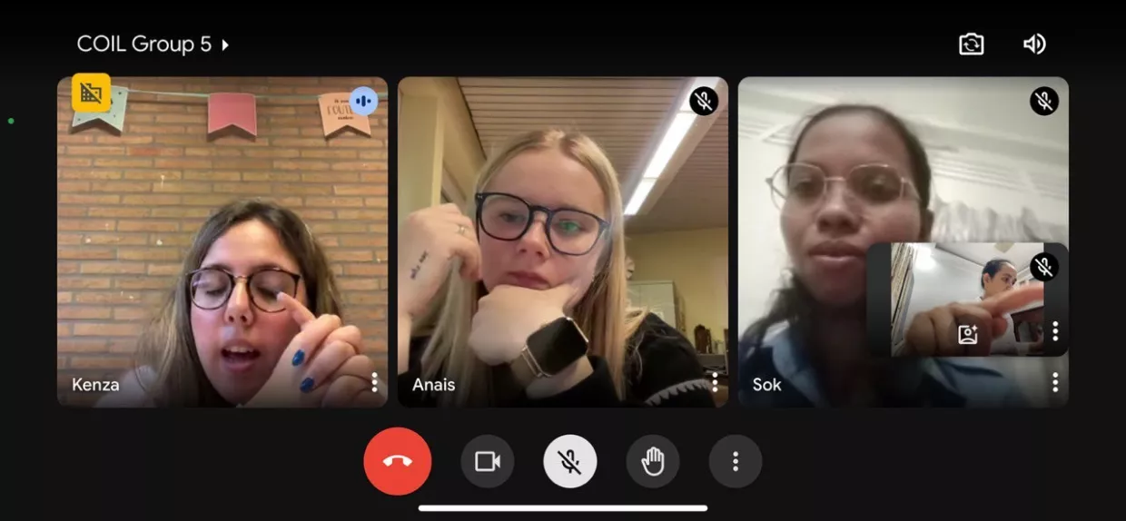 A video call with three people, each in their own video window. The mood appears focused. One person has a background with brick and banners.