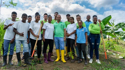 A diverse group of eleven people stands smiling in a lush garden.