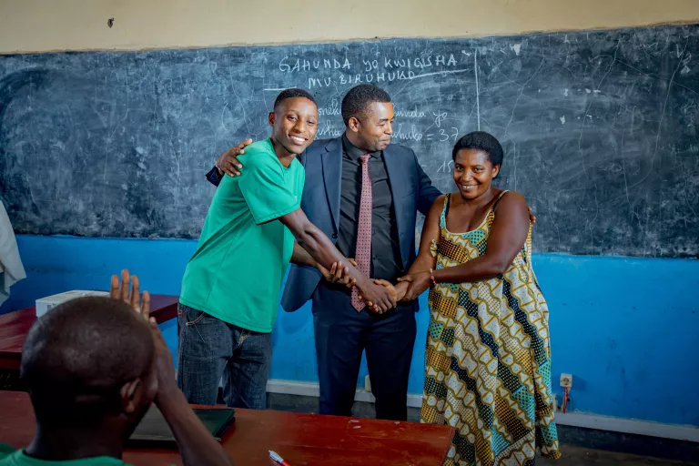 Three participants of the African Centre of School Leadership pictured in Rwandan classroom shaking hands and smiling