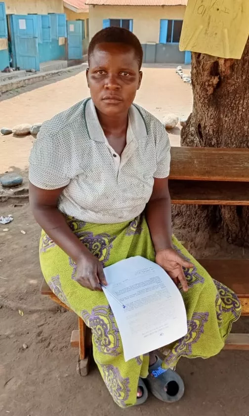 Grace is sitting under a tree outside, wearing a yellow long skirt.
