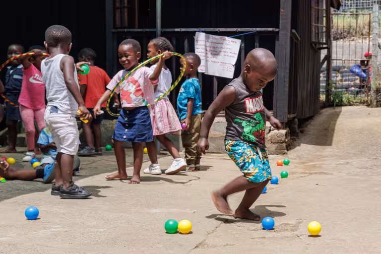 Young children play outdoors with hoops and colorful balls in a school playground.