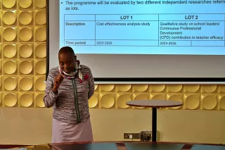 A person presents in front of a screen displaying enthusiastically.