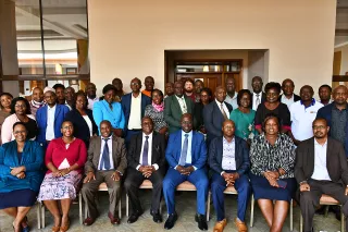 A diverse group of 34 people, mixed genders, in business attire, pose indoors for a group photo.