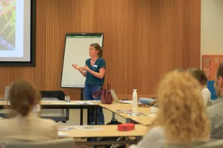 A woman speaking enthusiastically in front of a group. 