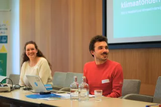 Two people smiling and engaged in front of a large screen.