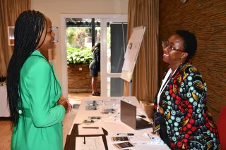 Two women having a discussion at a table covered with documents and a laptop.