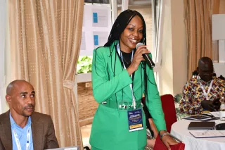 A woman in a bright green suit speaks into a microphone.
