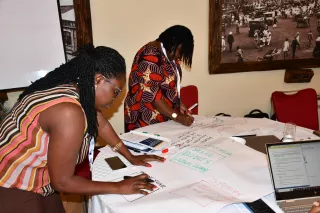 Two women collaboratively work around a table, writing on large paper.