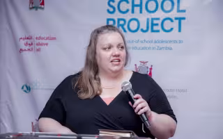 Woman speaking through a microphone, standing in front of a banner that says Digital School Project