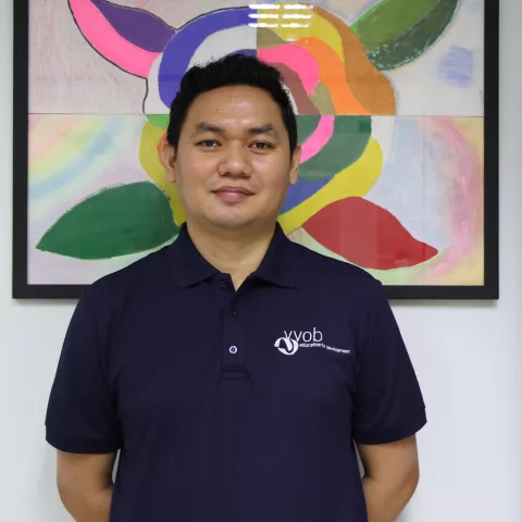 Roger wearing a navy VVOB polo shirt, standing in front of a colourful abstract painting.