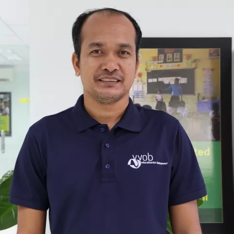 Virak wearing a navy VVOB polo shirt, standing in front of a colourful picture.