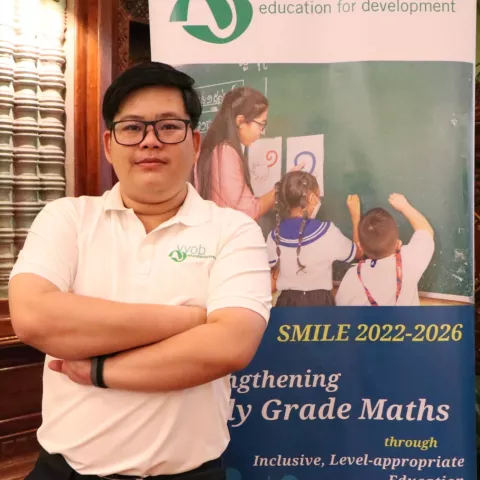 Sotheavny wearing a white VVOB polo shirt, standing in front of a VVOB banner.