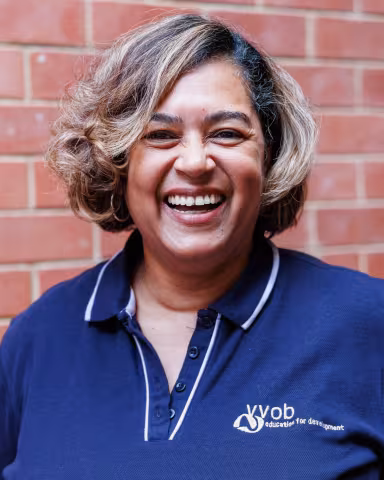 Chantal smiling in a navy polo shirt stands against a brick wall. Her expression is warm and friendly.
