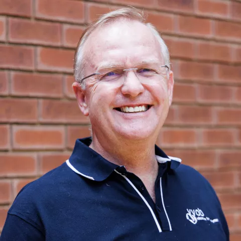 Gerrit smiling in a navy polo shirt stands against a brick wall. His expression is warm and friendly.