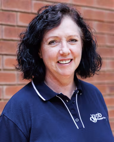 Laetitia smiling in a navy polo shirt stands against a brick wall. Her expression is warm and friendly.