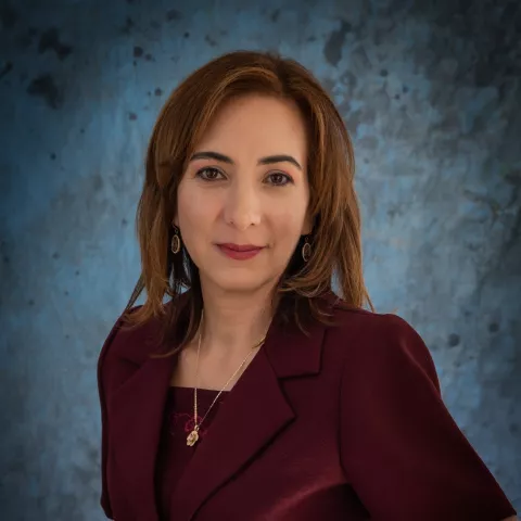  María Fernanda wearing a burgundy blazer stands against a textured blue backdrop.