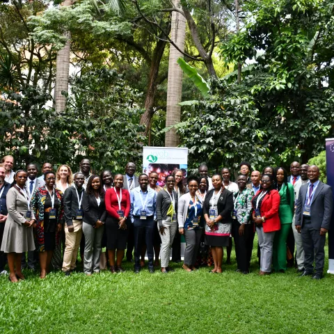A diverse group of people standing on grass, smiling, next to two large banners.