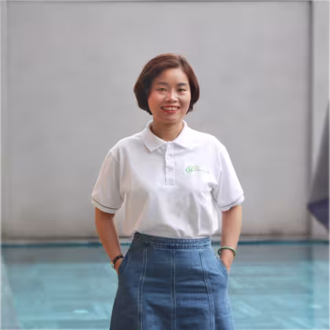 Oanh wearing a white polo shirt and denim skirt stands by a pool. The mood is friendly and casual, set against a plain background.