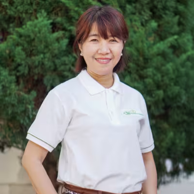 Phuc smiles warmly, wearing a white VVOB polo shirt. She stands against a backdrop of lush green foliage.