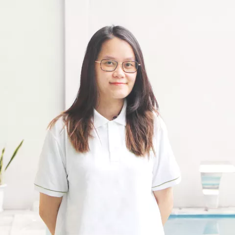 Huong smiles softly. She is wearing a white VVOB polo shirt and glasses. She stands in front of a white background. 