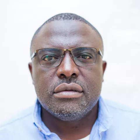 Aaron is wearing a blue shirt and glasses. The background is plain white.