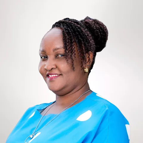 Abigail is wearing a blue shirt with white polka dots. She is smiling. The background is light gray.