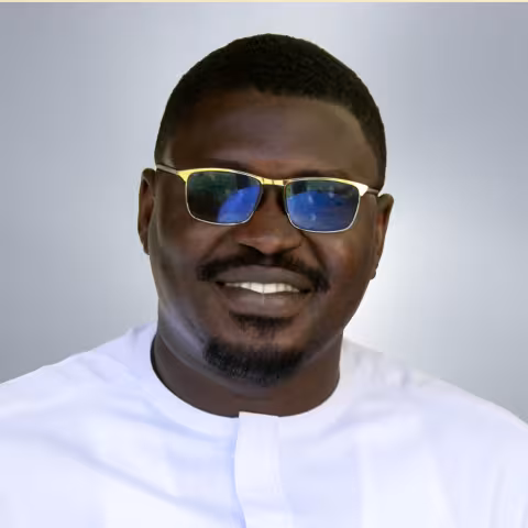 Alex is wearing glasses with blue lenses and a white shirt. He smiles warmly against a neutral background.