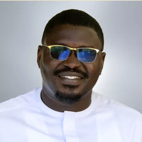 Alex is wearing glasses with blue lenses and a white shirt. He smiles warmly against a neutral background.