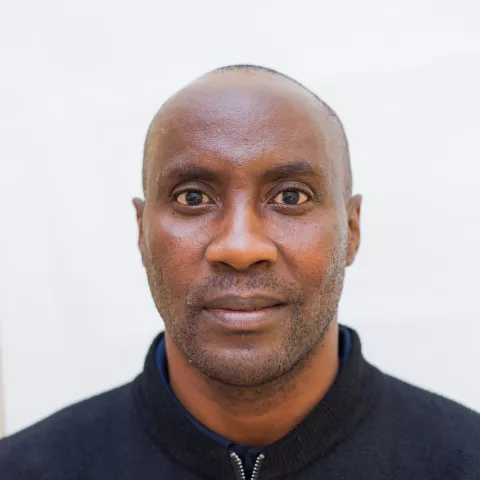 Andrew has a neutral expression and looks directly at the camera. He's wearing a black zip-up jacket with a subtle logo. The background is plain white.