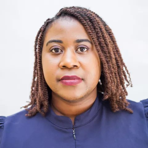 Annet has braided hair and wears a navy blue top, looking directly at the camera with a calm expression. The background is a soft white.