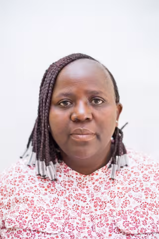 Charity is wearing a red patterned shirt. Her expression is neutral. The background is plain white.  