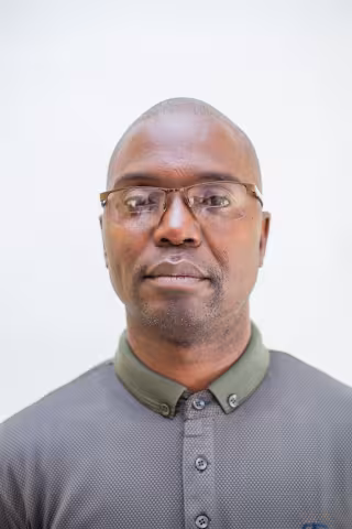 Charles is wearing glasses and a dark green and grey shirt. The background is plain white.