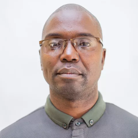 Charles is wearing glasses and a dark green and grey shirt. The background is plain white.