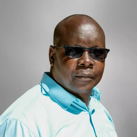 Collins is in sunglasses and wearing a light blue shirt. He stands against a neutral gray background.