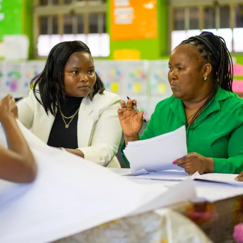 Female eachers sit together at a classroom table discussing notes during a professional learning community.
