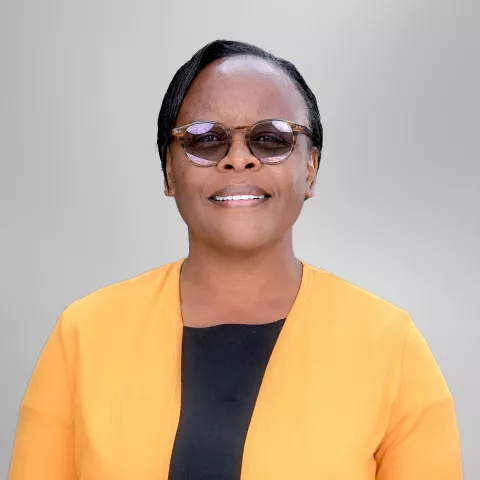 Everlyne n wearing sunglasses and an orange and black outfit against a light gray background.