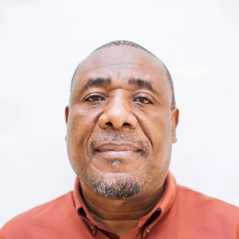 Fist is wearing a red shirt. He is smiling softly at the camera. The background is plain white. 